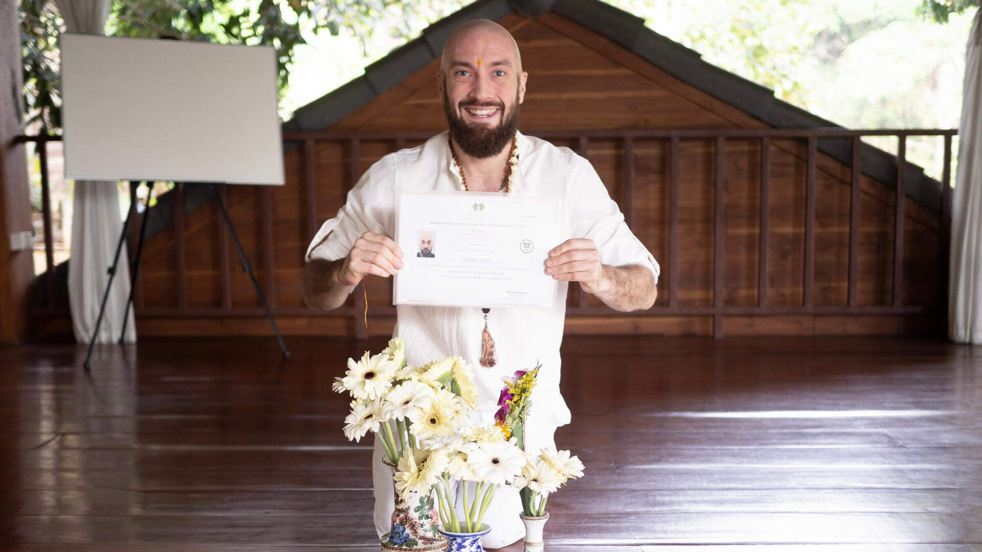 A yoga teacher holding up their training certificate upon completion at Yoga Vidya Mandiram